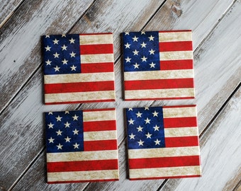 May include: Set of four square ceramic coasters featuring a distressed American flag design. Each coaster has a red, white, and blue color scheme with a faded look.