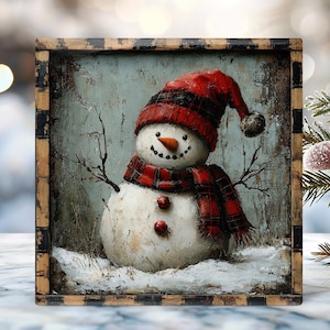 May include: A framed painting of a snowman wearing a red plaid hat and scarf. The snowman has a carrot nose, coal eyes, and a smiling mouth. The artwork is set against a light blue background with a distressed finish.