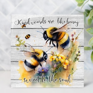 May include: Square wooden block with a watercolor painting of bees and flowers. The block features the text "Kind words are like honey, sweet to the soul" in a script font. The artwork has a rustic, farmhouse style.