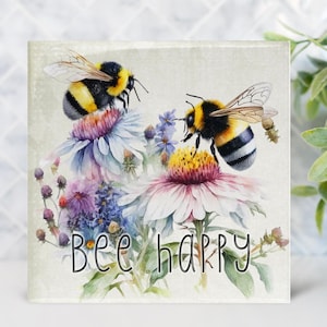 May include: A white square glass coaster with a watercolor painting of two bumblebees on flowers. The text "Bee Happy" is written in black at the bottom of the coaster.