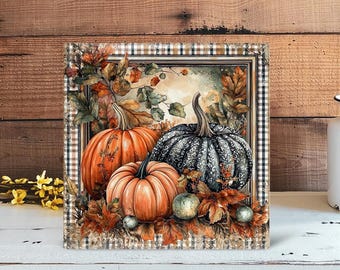 May include: A square canvas print featuring a watercolor painting of three pumpkins. Two are orange, and one is dark gray with a floral pattern. The pumpkins are surrounded by fall leaves and small green gourds, set within a plaid frame.