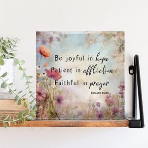 May include: A square floral art print with the text "Be joyful in hope, Patient in affliction, Faithful in prayer" against a soft, watercolor-style background. The print features pink and orange flowers.