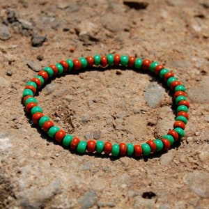 May include: A green and orange beaded bracelet. The bracelet is made of small, round beads that are strung together in a repeating pattern.