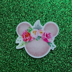 Peut inclure: Des oreilles de souris roses avec une couronne florale de fleurs roses, blanches et vertes. Les oreilles sont sur un fond de paillettes vertes.