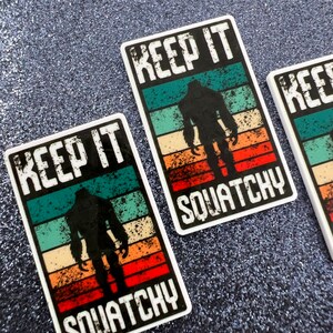 May include: Two white stickers with a retro-style design featuring a silhouette of Bigfoot. The stickers say "Keep It Squatchy".