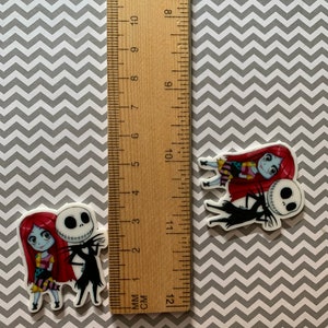 Puede incluir: Dos personajes de dibujos animados, Jack Skellington y Sally de Pesadilla antes de Navidad, se representan en una imagen de primer plano. Ambos sonr&iacute;en y se toman de la mano. Los personajes est&aacute;n impresos sobre un fondo blanco.