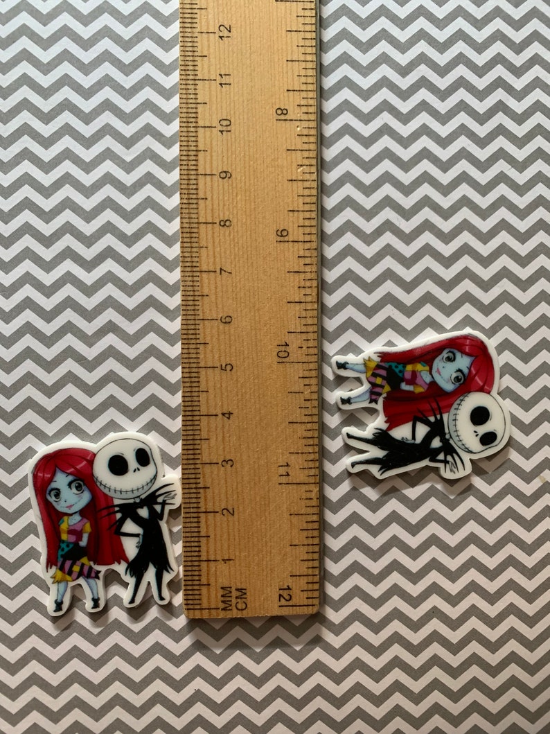 Puede incluir: Dos personajes de dibujos animados, Jack Skellington y Sally de Pesadilla antes de Navidad, se representan en una imagen de primer plano. Ambos sonr&iacute;en y se toman de la mano. Los personajes est&aacute;n impresos sobre un fondo blanco.