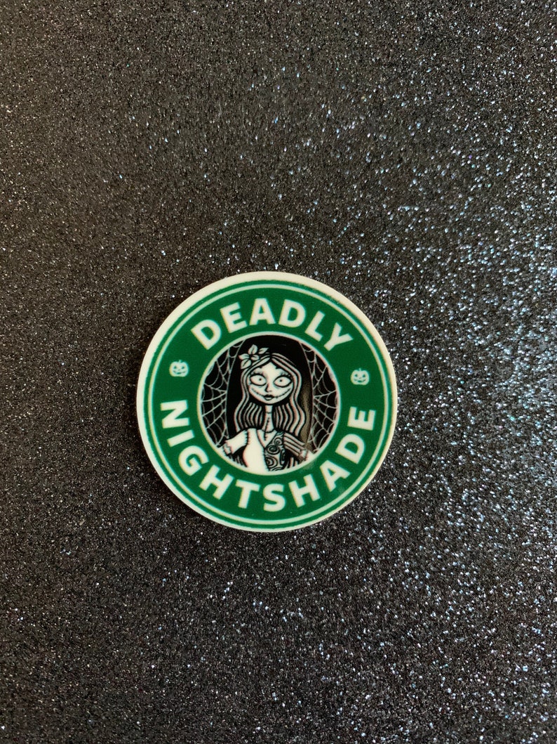 Puede incluir: Una pegatina redonda verde y blanca con el texto "Deadly Nightshade" en un c&iacute;rculo alrededor de una imagen de dibujos animados de una mujer con el pelo largo y negro y un vestido blanco.