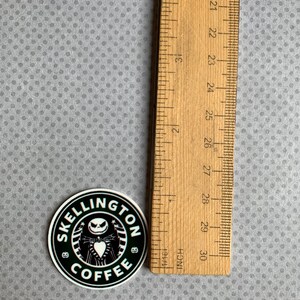 May include: Black and white sticker with a coffee cup logo that says "Skellington Coffee". The logo features a cartoon character with a black and white striped shirt and a black bow tie. The sticker is approximately 2 inches in diameter.