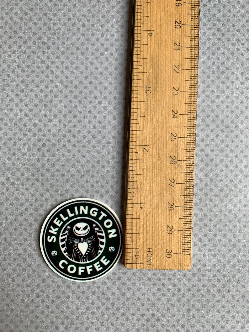 May include: Black and white sticker with a coffee cup logo that says "Skellington Coffee". The logo features a cartoon character with a black and white striped shirt and a black bow tie. The sticker is approximately 2 inches in diameter.