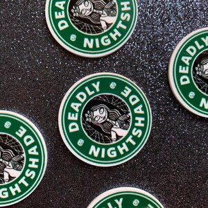 Puede incluir: Cuatro pegatinas redondas verdes y blancas con el texto "Deadly Nightshade" y una imagen de dibujos animados de una ni&ntilde;a con cabello negro y un vestido blanco. Las pegatinas tienen un dise&ntilde;o de telara&ntilde;a.