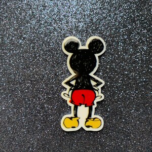 Peut inclure: Un personnage de dessin animé noir et blanc avec de grandes oreilles, un short rouge et des chaussures jaunes. Le personnage est debout sur un fond noir scintillant.