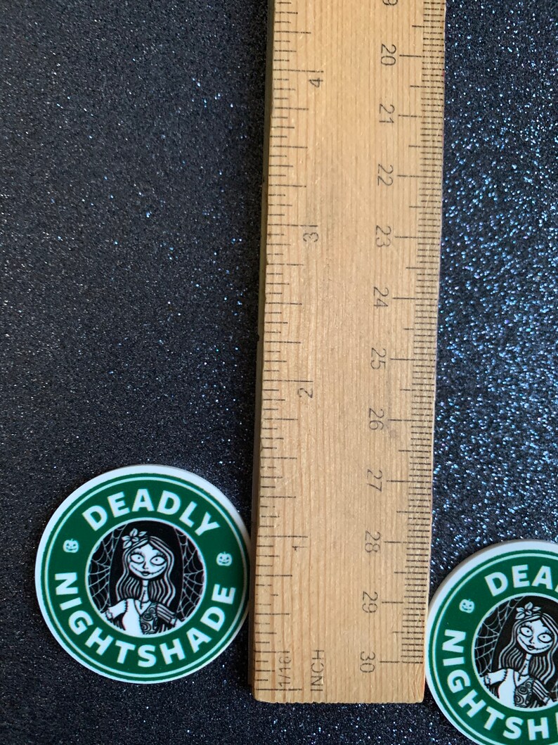 Puede incluir: Dos pegatinas redondas verdes y blancas con una ilustraci&oacute;n en blanco y negro de un personaje con un dise&ntilde;o de telara&ntilde;a y el texto "DEADLY NIGHTSHADE".
