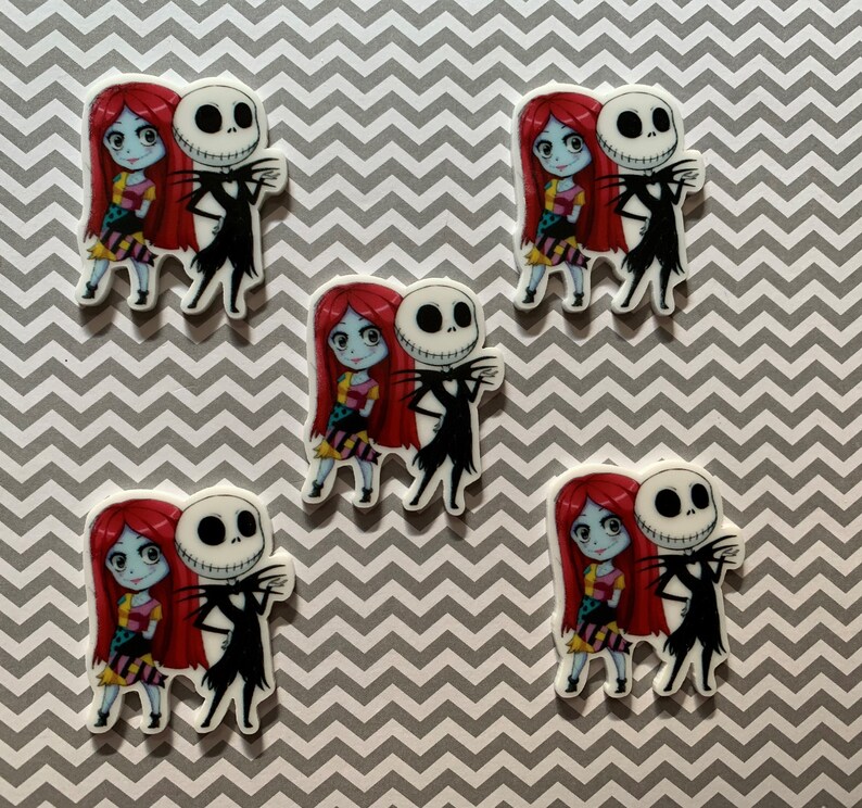 Puede incluir: Cinco pegatinas de personajes de dibujos animados coloridos con Jack Skellington y Sally de la pel&iacute;cula Pesadilla antes de Navidad. Las pegatinas est&aacute;n sobre un fondo de patr&oacute;n de chevron gris y blanco.