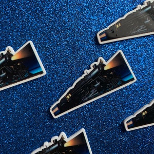 May include: Five white stickers with a black and white image of a train engine with a headlight on. The train is on a dark blue background.