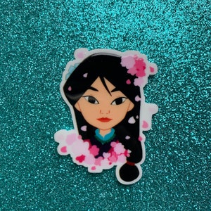 May include: A sticker featuring a cartoon illustration of a woman with black hair and a blue and pink dress. The woman is surrounded by pink flower petals.