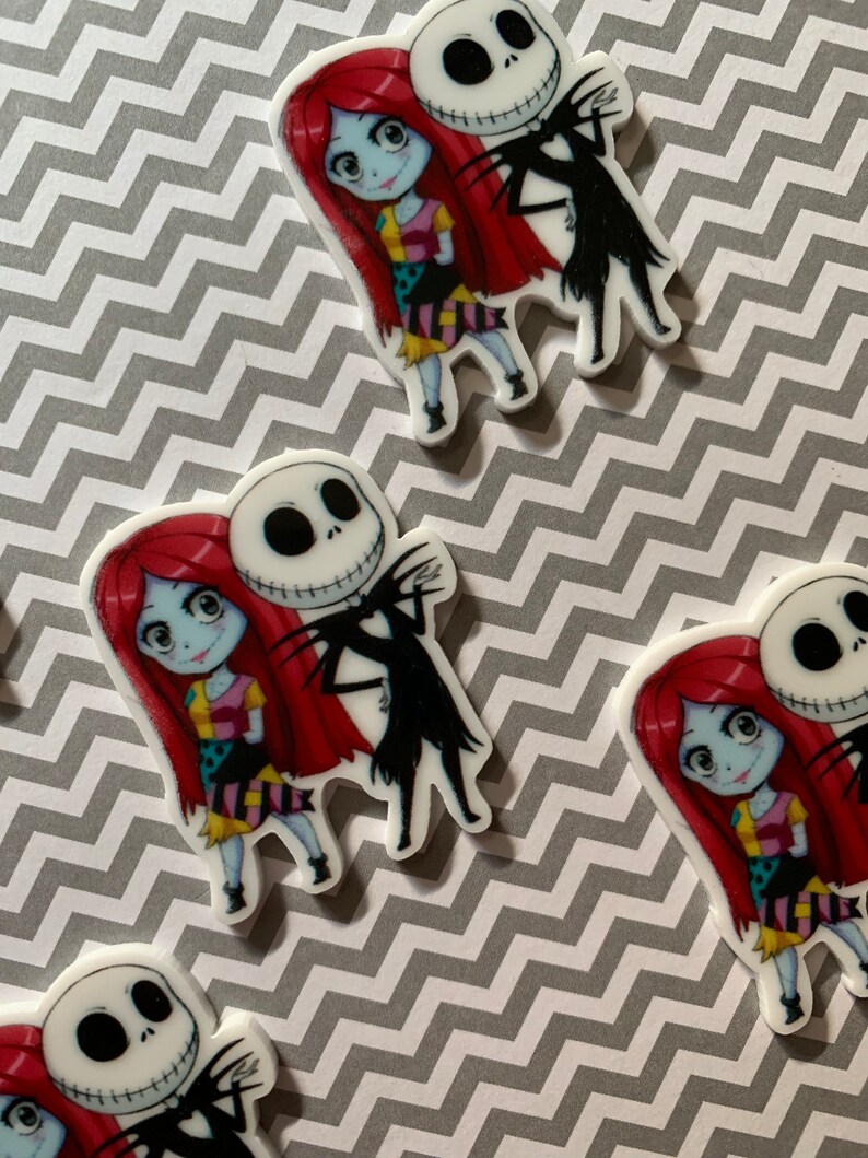 Puede incluir: Una imagen de primer plano de dos personajes de dibujos animados, Jack Skellington y Sally de Pesadilla antes de Navidad. Jack lleva su traje negro caracter&iacute;stico y tiene una amplia sonrisa, mientras que Sally lleva su vestido de retazos y tiene una expresi&oacute;n dulce. Los personajes est&aacute;n de pie uno al lado del otro, con el brazo de Jack alrededor de la cintura de Sally.