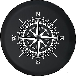 May include: Black spare tire cover featuring a white compass rose design. The compass rose includes the cardinal directions: North, South, East, and West, along with intermediate directions. The cover is round and designed to fit a spare tire.