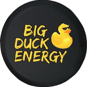 May include: Black circular design featuring the text "BIG DUCK ENERGY" in yellow, outlined in black. A yellow rubber duck wearing sunglasses is to the right of the text. The design is likely for a spare tire cover.