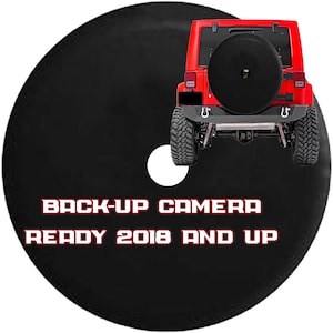 May include: Black spare tire cover with the text "BACK-UP CAMERA READY 2018 AND UP" in red and white. A red Jeep is in the background. The cover has a white circle cut out.