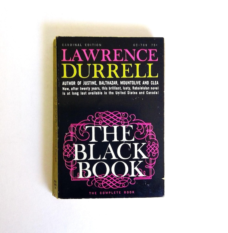 May include: A vintage paperback book titled "The Black Book" by Lawrence Durrell. The cover is black with pink and white text and design elements. The book is a Cardinal Edition.