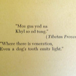 May include: A page from a book with a Tibetan proverb printed in black ink. The quote, in English, reads: "Where there is veneration, Even a dog's tooth emits light."