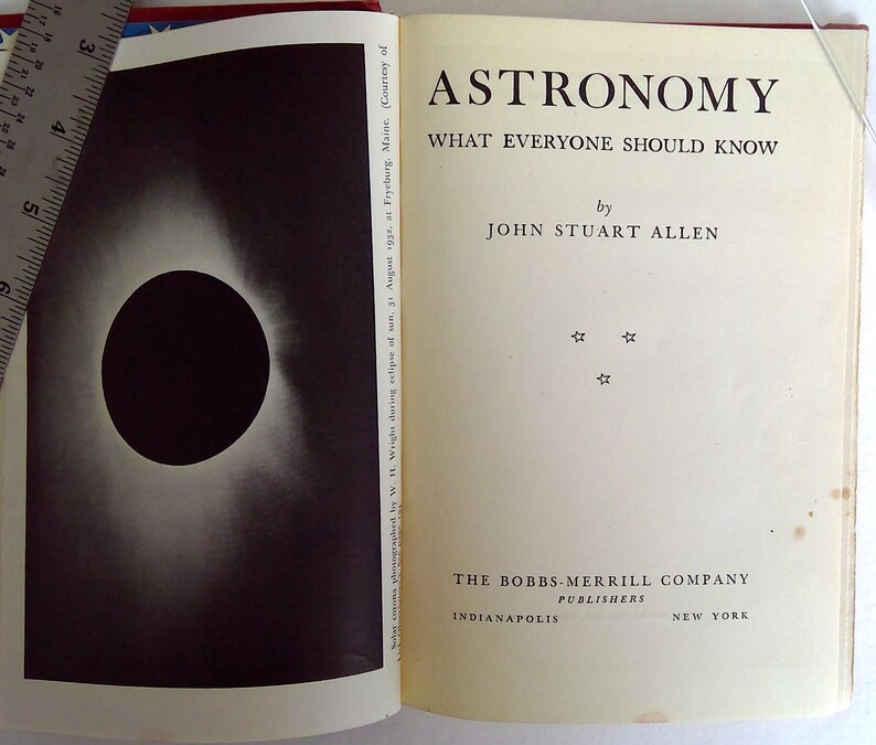 Puede incluir: Libro abierto titulado "Astronom&iacute;a Lo que todos deber&iacute;an saber" por John Stuart Allen. La p&aacute;gina izquierda presenta una imagen en blanco y negro de un eclipse solar. El libro es publicado por The Bobbs-Merrill Company.
