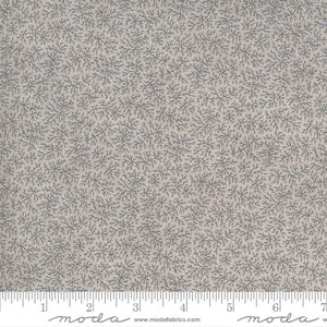 May include: A close-up of a beige fabric with a repeating pattern of small, dark grey, stylised branches. The fabric has a subtle texture and a slightly faded appearance. The fabric is marked with a ruler in inches, with the text "moda" printed on the ruler.