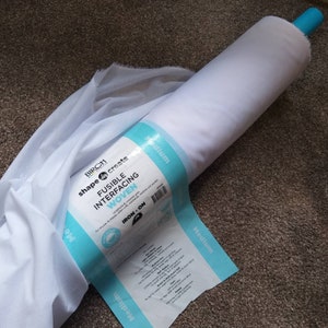 May include: A roll of white fusible interfacing fabric with a blue label that reads "Birch shape create Fusible Interfacing Woven Iron-On Medium".