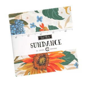 Może przedstawiać: Biała tkanina z kwiatowym nadrukiem przedstawiającym słoneczniki, niebieskie kwiaty i zielone liście. Tkanina jest oznaczona "SUNDANCE by CRYSTAL MANNING" i ma linijkę o długości 20,3 cm.