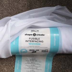 May include: A white roll of fusible interfacing fabric for sewing projects. The label reads "Birch Creative shape to create Fusible Interfacing Woven Lengthwise & crosswise grain For blouses & dresses, collars cuffs, waistbands, necklines and pockets Machine Iron-On STCOM4"