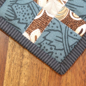 May include: A close-up of a blue and brown fabric with a black border. The fabric is made of patchwork squares with different patterns. The fabric is likely a quilt or a table runner.