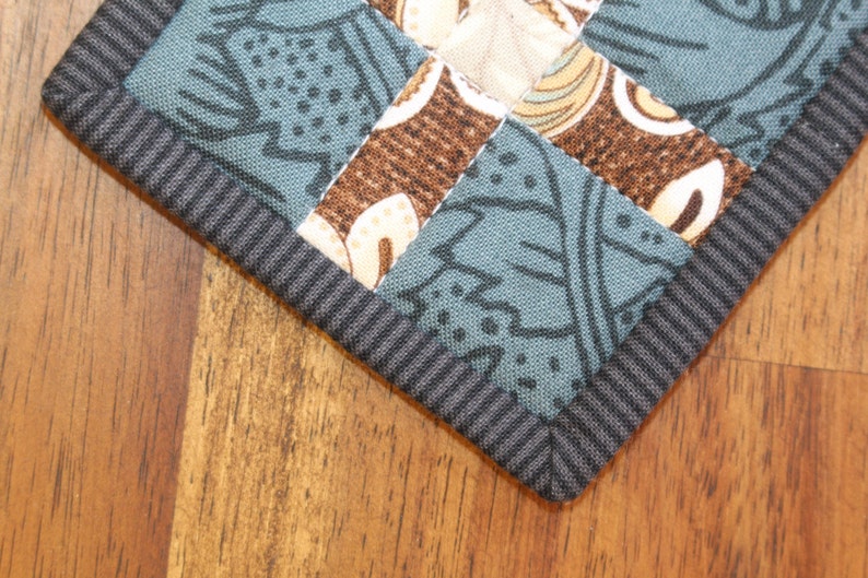 May include: A close-up of a blue and brown fabric with a black border. The fabric is made of patchwork squares with different patterns. The fabric is likely a quilt or a table runner.