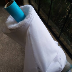 May include: A white fabric roll with a blue cardboard tube. The fabric is rolled up and the tube is sticking out of the roll.