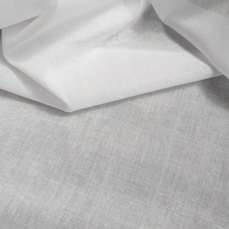 May include: White fabric with a smooth, silky texture. The fabric is folded in half, revealing a slightly textured underside.