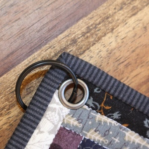 May include: Close-up of a black metal ring attached to a gray and black striped fabric with a silver metal grommet.