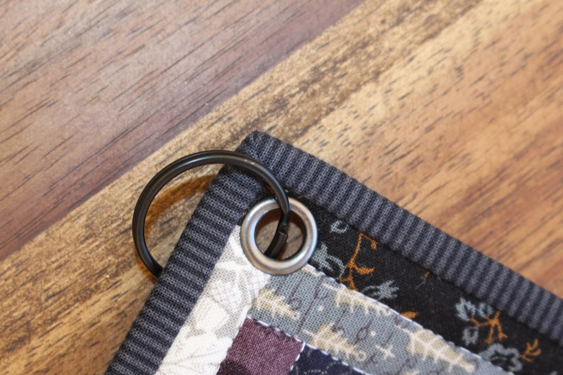 May include: Close-up of a black metal ring attached to a gray and black striped fabric with a silver metal grommet.