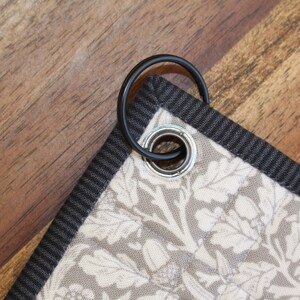 Może przedstawiać: Zbliżenie czarnego materiału z białym wzorem kwiatowym. Materiał ma przymocowany czarny metalowy pierścień.