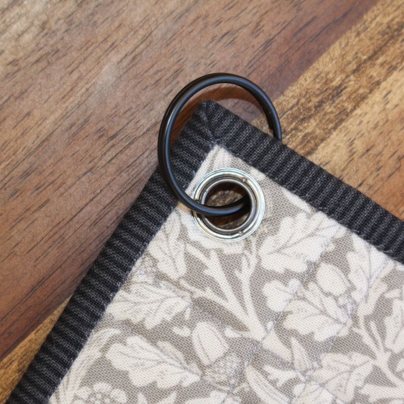 Może przedstawiać: Zbliżenie czarnego materiału z białym wzorem kwiatowym. Materiał ma przymocowany czarny metalowy pierścień.