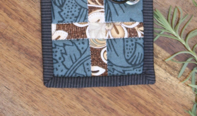 May include: A small, blue and brown fabric patchwork with a black border. The fabric has a floral pattern.