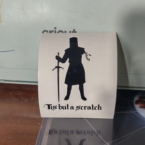 Puede incluir: Una silueta negra de un caballero sosteniendo una espada con el texto "Tis but a scratch" debajo.