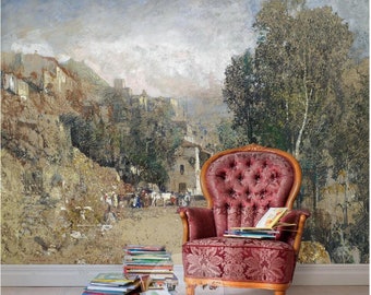 Op de afbeelding: Een vintage fauteuil met een rode fluwelen bekleding en knopen zit voor een groot schilderij dat een landschap met een dorp in de verte toont. Het schilderij is in een gedempte kleurenpalet met tinten bruin, groen en blauw. Een stapel boeken ligt op de vloer naast de stoel.