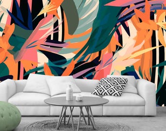 May include: A white couch with a patterned pillow sits in front of a wall with a colorful abstract tropical print. The couch is in a living room setting with a gray coffee table and a green ottoman.