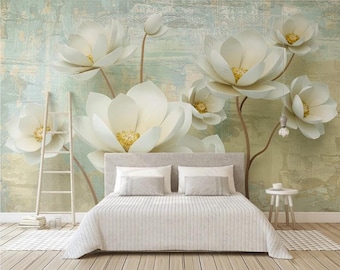 May include: A white bed with a white duvet cover and two white pillows sits in front of a wall mural featuring large white flowers with yellow centers on a light blue and green background.