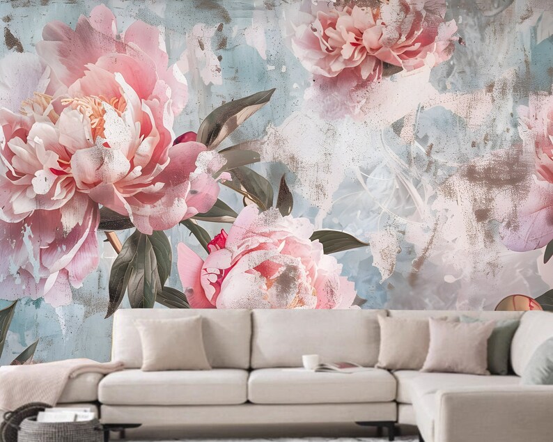 Op de afbeelding: Een vintage-stijl bloemenbehang met grote roze pioenen met groene bladeren op een lichtblauwe en grijze textuur achtergrond. Een witte hoekbank staat op de voorgrond.