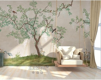 May include: A white swing chair hangs in front of a wall mural depicting a stylized tree with white blossoms and birds. The mural is painted on a beige background. The swing chair has a woven frame and a white cushion.
