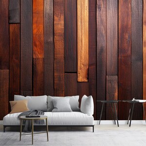 Può includere: Un divano bianco con una coperta marrone si trova di fronte a una parete con un design a pannelli di legno. La parete è realizzata con assi di legno marrone scuro di diverse larghezze e tonalità. Due tavolini neri con piano rotondo sono posizionati su entrambi i lati del divano.