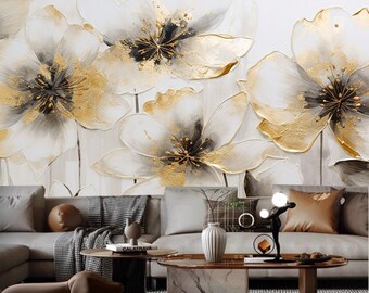 May include: A white wall with a large abstract floral painting featuring white, gold, and black flowers. The painting is above a gray sectional sofa with brown throw pillows and a coffee table with a book on it.