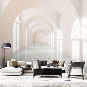 Puede incluir: Un pasillo blanco y beige con puertas arqueadas y un suelo de baldosas blancas. El pasillo está iluminado por la luz del sol que entra por las ventanas. El pasillo está vacío, excepto por algunos muebles, como un sofá, una mesa de centro y una silla.