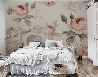 May include: A white bed with a white duvet and a gray throw blanket. The bed is in front of a wall with a floral wallpaper featuring pink roses and green leaves.